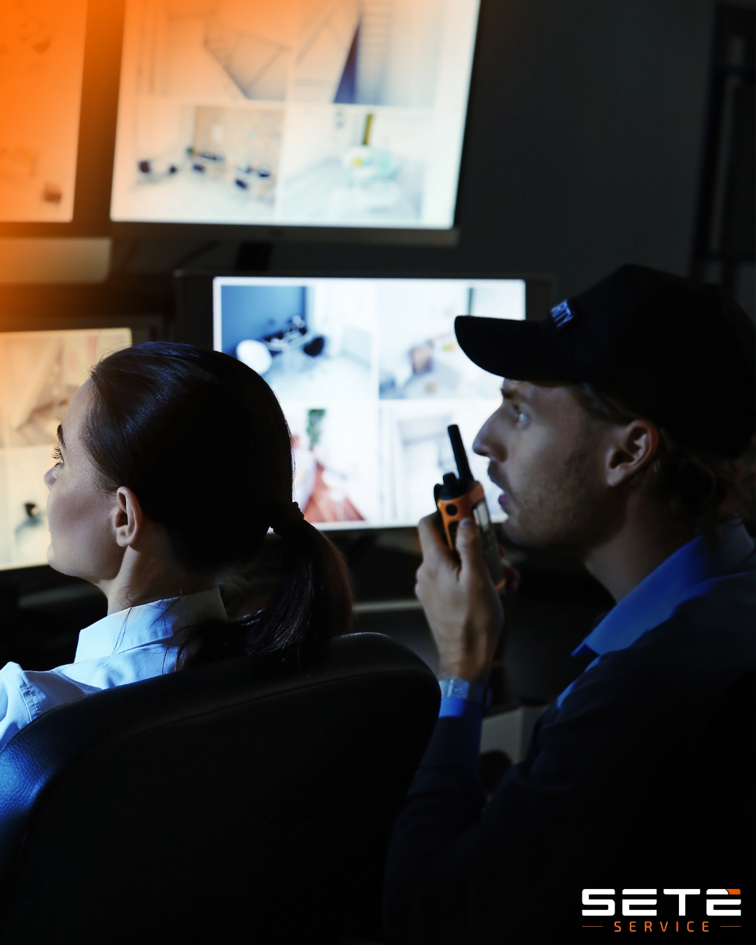 Seguranças observam telas de monitoramento; homem fala ao rádio enquanto mulher acompanha as imagens ao lado.